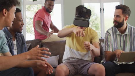 Happy-diverse-male-friends-using-vr-headset-and-talking-in-living-room