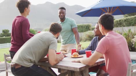 Happy-diverse-male-friends-talking-and-drinking-beer-in-garden-on-sunny-day