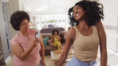 Happy-diverse-female-friends-using-smartphone-and-dancing-in-living-room