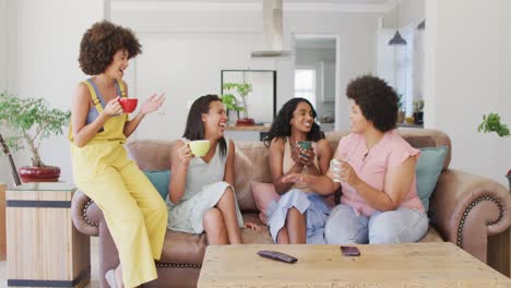 Happy-diverse-female-friends-sitting-on-sofa-in-living-room,-talking-and-smiling