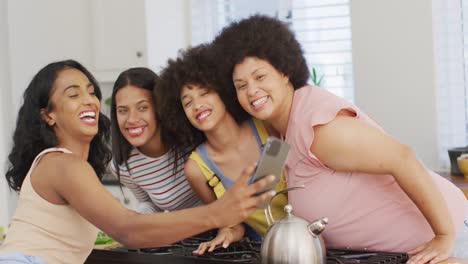 Happy-diverse-female-friends-taking-selfies-using-smartphone-in-kitchen