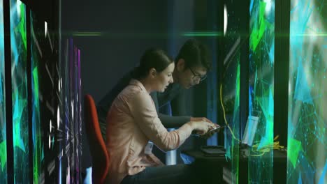 Animation-of-shapes-over-diverse-man-and-woman-working-on-laptop-in-server-room