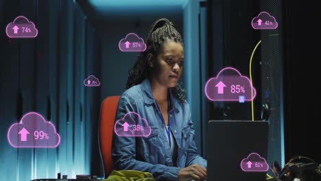 Animation-of-cloud-with-uploading-over-african-american-woman-working-on-laptop-in-server-room