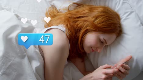 Animation-of-social-media-reactions-over-caucasian-woman-using-smartphone-in-bed