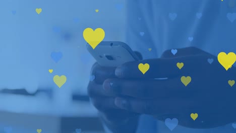 Animation-of-yellow-and-blue-hearts-floating-over-hands-of-biracial-man-using-smartphone