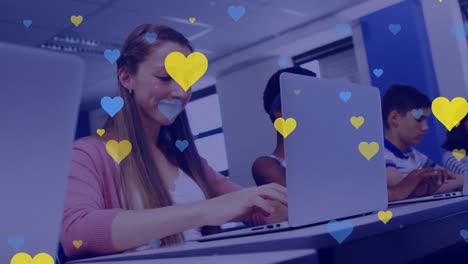 Animation-of-blue-and-yellow-hearts-falling-over-caucasian-girl-using-laptop-at-school