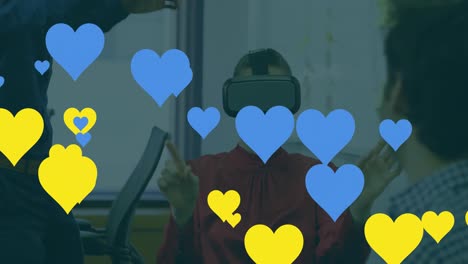 Animation-of-blue-and-yellow-hearts-floating-over-caucasian-men-testing-vr-headset