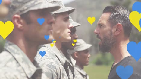 Animation-of-yellow-and-blue-hearts-floating-over-diverse-male-soldiers-and-trainer