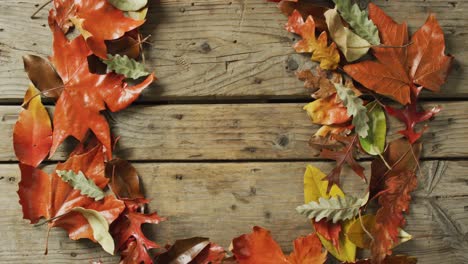 Video-of-wreath-made-of-fall-leaves-lying-on-wooden-background