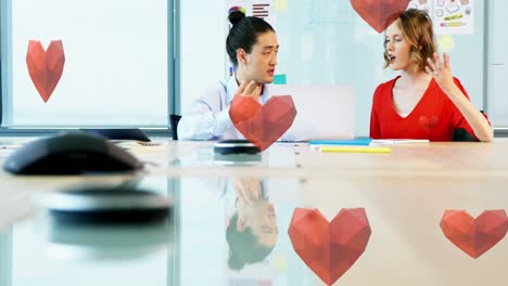 Animation-of-hearts-falling-over-diverse-coworkers-talking-in-office