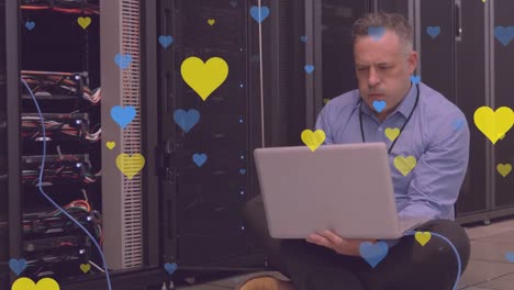 Animation-of-hearts-and-caucasian-businessman-using-laptop-in-server-room