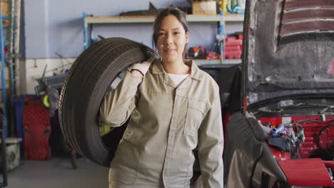 Video-of-happy-biracial-female-car-mechanic-holding-tyre