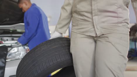 Video-of-midsection-of-biracial-female-car-mechanic-holding-tyre