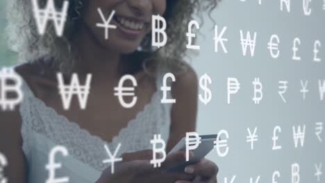 Animation-of-currency-symbols-over-african-american-businesswoman-using-smartphone