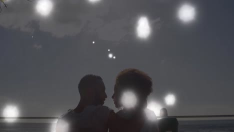 Animation-of-glowing-spots-of-light-over-african-american-couple-embracing-each-other-at-the-beach