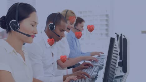 Multiple-red-heart-icons-floating-against-team-of-diverse-customer-care-executives-working-at-office
