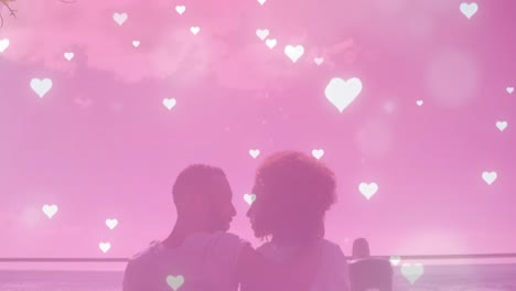 Mehrere-Leuchtende-Herzsymbole-Fallen-über-Ein-Afroamerikanisches-Paar,-Das-Sich-Am-Strand-Küsst