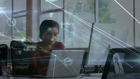 Animation-of-connections-over-biracial-woman-working-on-laptop-in-office