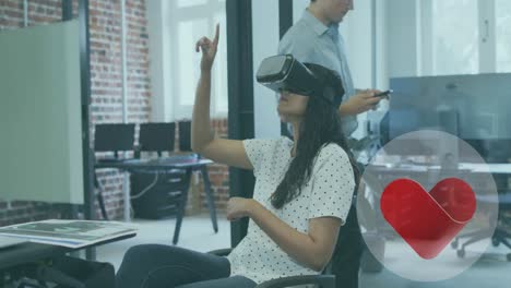 Animation-of-heart-icon-over-biracial-woman-wearing-vr-headset-in-office