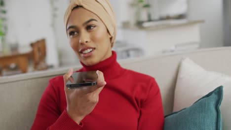 Video-Einer-Glücklichen-Gemischtrassigen-Frau-Im-Hijab,-Die-Auf-Dem-Sofa-Sitzt-Und-Telefoniert