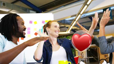 Red-heart-icon-over-diverse-office-colleagues-high-fiving-each-other-at-office