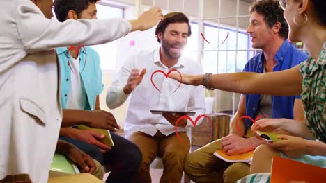 Red-heart-icons-falling-over-diverse-office-colleagues-stacking-their-hands-together-at-office