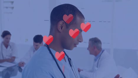Animation-of-hearts-floating-over-happy-biracial-male-doctor-making-notes