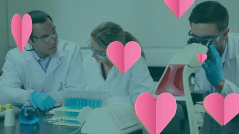 Animation-of-hearts-falling-over-diverse-female-and-male-lab-workers-with-microscope