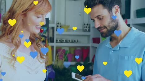 Animation-Von-Blauen-Und-Gelben-Herzen-über-Verschiedenen-Menschen,-Die-Mit-Dem-Smartphone-Bezahlen