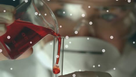 Animation-of-dots-floating-over-caucasian-female-lab-worker-pouring-liquid-into-glasses