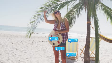 Animation-of-social-media-reactions-over-happy-caucasian-woman-standing-under-palm-on-beach