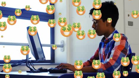 Multiple-money-eyes-face-emojis-floating-over-indian-boy-using-computer-at-school