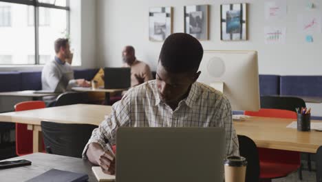 African-american-businessman-sitting-at-table-and-using-laptop-at-office