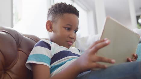 Video-Eines-Glücklichen-Afroamerikanischen-Jungen,-Der-Auf-Dem-Sofa-Sitzt-Und-Ein-Tablet-Benutzt