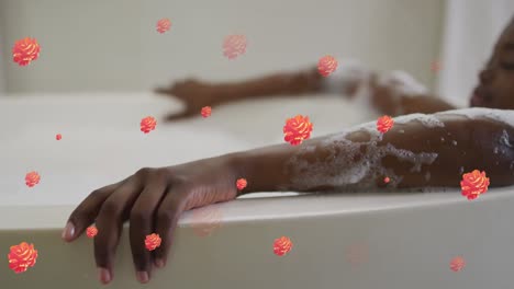 Animation-of-flower-icons-over-african-american-woman-taking-bath