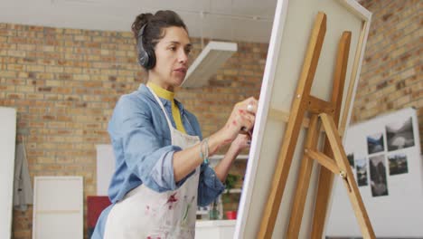 Video-of-biracial-female-artist-in-headphones-painting-in-studio
