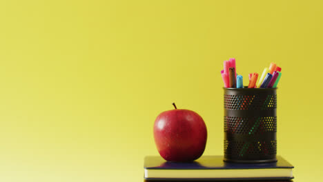 Video-of-crayons-in-container,-books-and-apple-on-yellow-surface