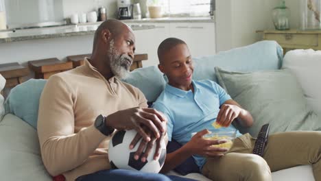 Video-Eines-Glücklichen-Afroamerikanischen-Vaters-Und-Sohnes,-Der-Gemeinsam-Chips-Isst-Und-Fernsieht