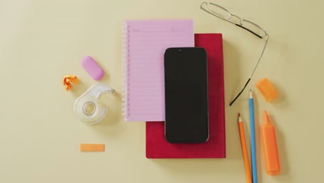 Video-of-smartphone-with-copy-space,-notebooks-and-school-equipment-on-yellow-background
