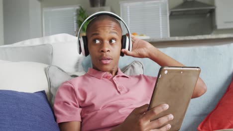 Video-Eines-Glücklichen-Afroamerikanischen-Jungen-Mit-Kopfhörern,-Der-Ein-Tablet-Auf-Dem-Sofa-Benutzt
