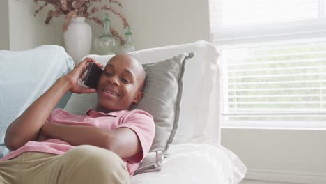 Fröhlicher-Afroamerikanischer-Junge,-Der-Im-Wohnzimmer-Auf-Dem-Smartphone-Spricht