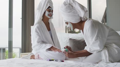 Video-of-happy-diverse-female-friends-moisturizing-with-face-masks-and-painting-nails
