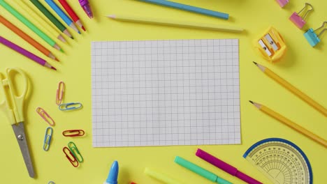 Video-of-school-supplies-and-notebooks,-paper-clips,-pens-over-yellow-background