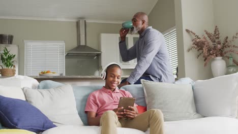 Video-of-happy-african-american-father-drinking-coffee-and-watching-tablet-with-son