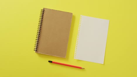 Video-of-notebook,-empty-sheet-with-copy-space-and-pencil-on-yellow-background