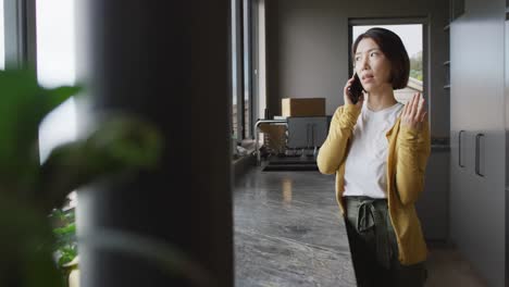 Mujer-Asiática-Vistiendo-Un-Jersey-Y-Hablando-Por-Teléfono-Inteligente-Solo-En-La-Cocina