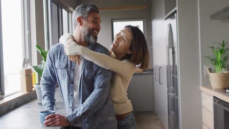 Happy-diverse-couple-wearing-casual-clothes-embracing-together-in-kitchen