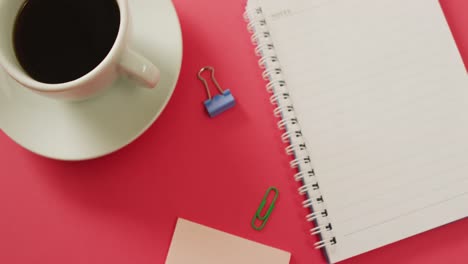 Video-of-notebook,-pins-and-coffee-lying-on-red-surface
