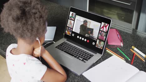 African-american-girl-using-laptop-for-video-call-with-male-teacher-and-class-on-screen