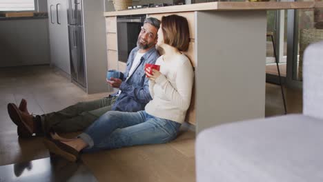 Happy-diverse-couple-sitting-in-kitchen-drinking-coffee-and-talking